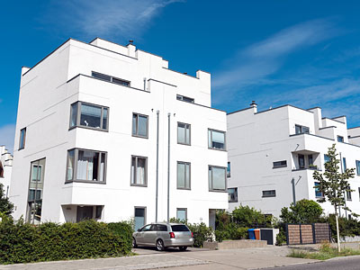 Weiße Wohnhäuser mit modernen Architekturmerkmalen, umgeben von Bäumen und einem Parkplatz.